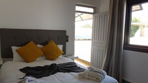 A neatly made bed with white and mustard pillows, a grey throw blanket, and a rolled towel. - Air-conditioned villa with private pool 15 minutes from the beaches (Essaouira)