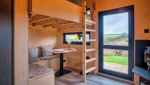 A cozy room with a wooden interior, a built-in desk, a window with a view of the outdoors, and a door leading outside.