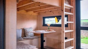 A cozy cabin interior with a wooden interior, a window with a view, a small table with a vase, and a ladder.