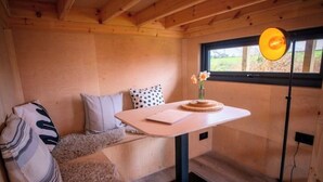 A cozy cabin interior with a wooden ceiling, a small table with a vase of flowers, a polka-dotted pillow, and a bench.