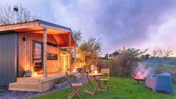 A wooden cabin with a covered porch, outdoor seating, and a fire pit.