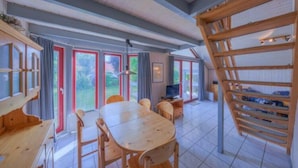 Habitación amplia con una gran mesa de comedor de madera, sillas y televisión. Cuenta con ventanas amplias y vistas al exterior.