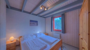 Un dormitorio con una cama de madera, una mesita de noche, una ventana con vistas y un cuadro en la pared.
