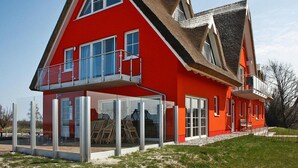 Una casa roja de dos pisos con un balcón, ventanas grandes y un tejado de paja.