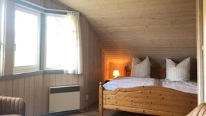 Puupaneloitu huone, jossa on sänky, tuoli ja ikkuna, jossa on verhot.