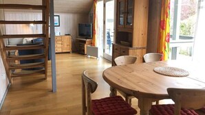 Tunnelmallinen mökin sisustus, jossa on puinen ruokapöytä, pehmustetut tuolit, televisio ja keittiöalue.