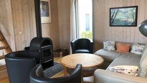 Tunnelmallinen huone, jossa on puukamiina, sohva, kaksi tuolia, pyöreä puupöytä ja ikkuna, josta on kaunis näkymä.