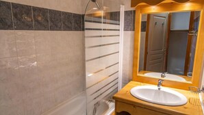 A bathroom with a glass shower enclosure, a wooden vanity with a sink, and a mirror with a wooden frame.