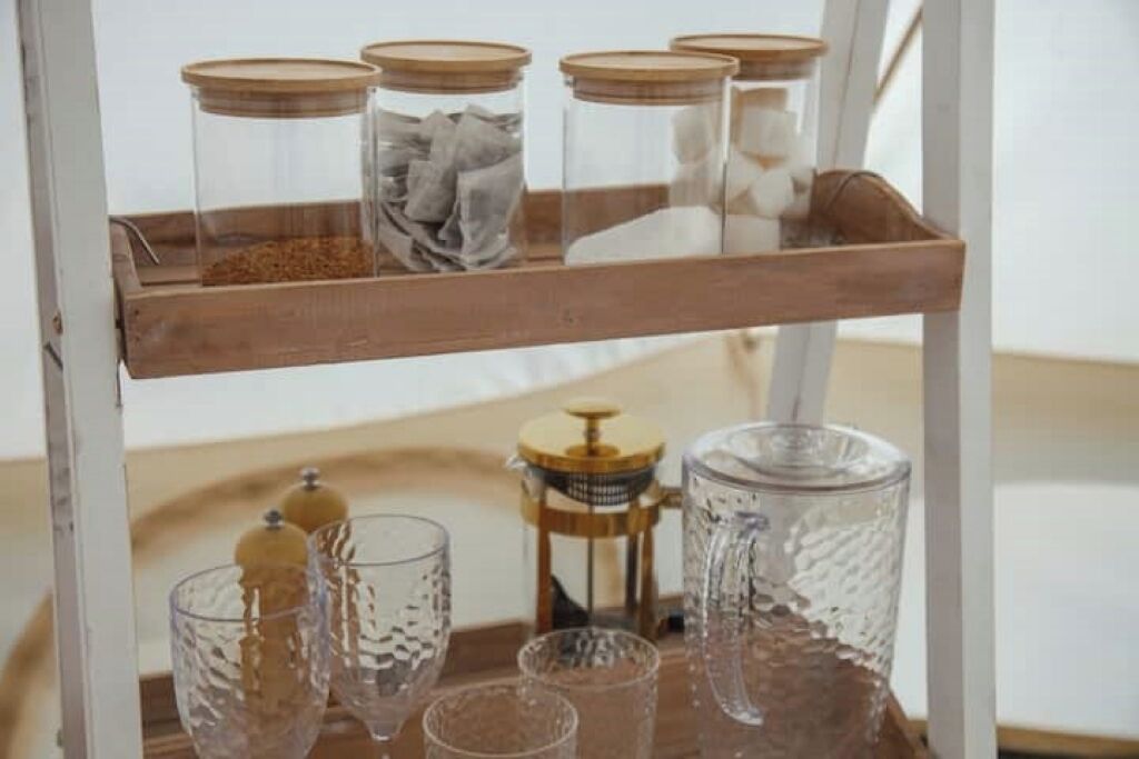Une étagère en bois avec des bocaux en verre et une cafetière à piston.