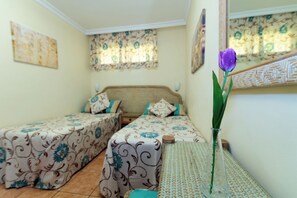 Un dormitorio con dos camas, un jarrón con una flor morada y cortinas estampadas.