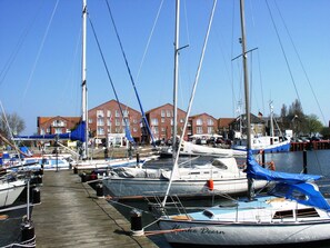 Una marina con diverse barche a vela ormeggiate, passerelle in legno e edifici sullo sfondo.