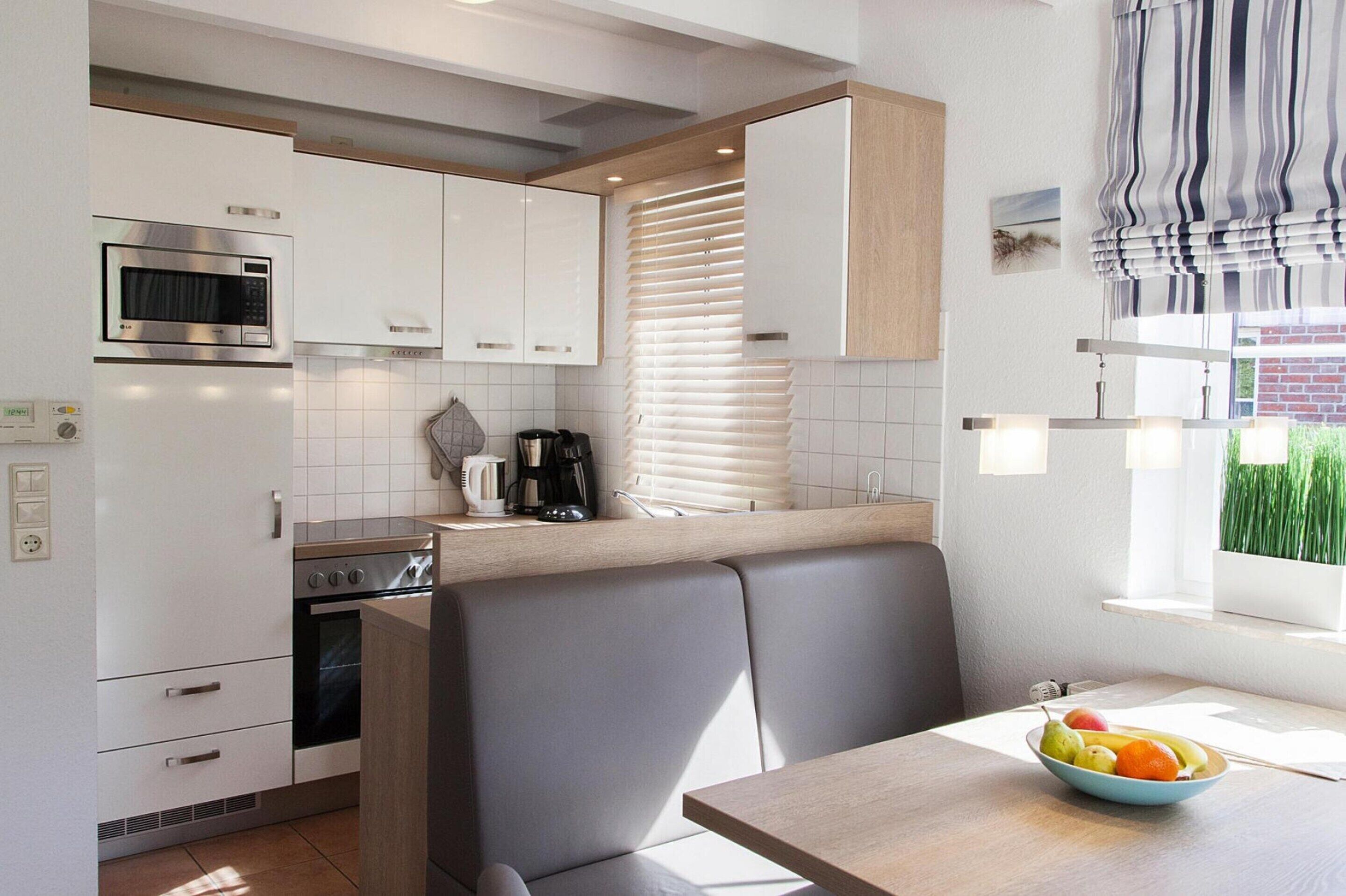 A modern kitchen with white cabinets, a built-in oven, a microwave, and a dining area with a table and chairs.