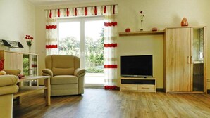 A living room with a sofa, armchair, TV stand, and wooden cabinet. - Ferienwohnung Landblick, Rastede (Rastede)