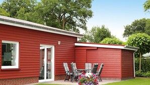 A red house with a patio, a sliding glass door, and a small garden with chairs and flowers. - Ferienwohnung Landblick, Rastede (Rastede)