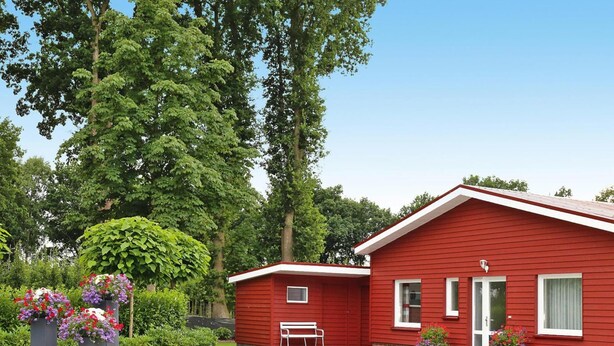 A red single-story house with a front porch, a small attached garage, and a well-maintained lawn. - Ferienwohnung Landblick, Rastede (Rastede)