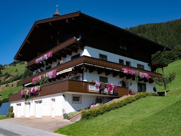 Un chalet à deux étages, doté de balcons ornés de fleurs, qui se dresse sur une colline.