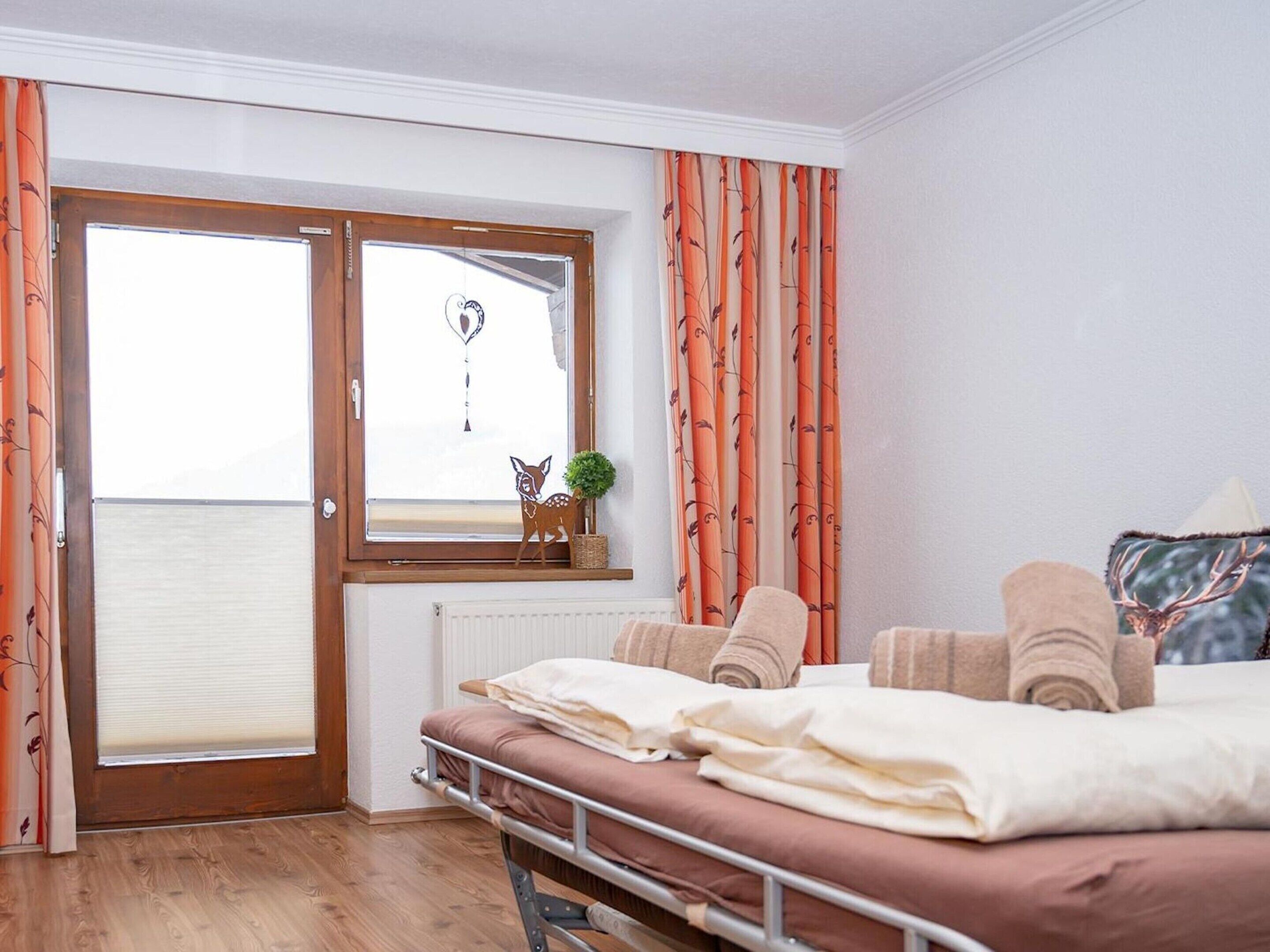A bedroom with a bed, a window with curtains, a radiator, and a small plant on the windowsill.
