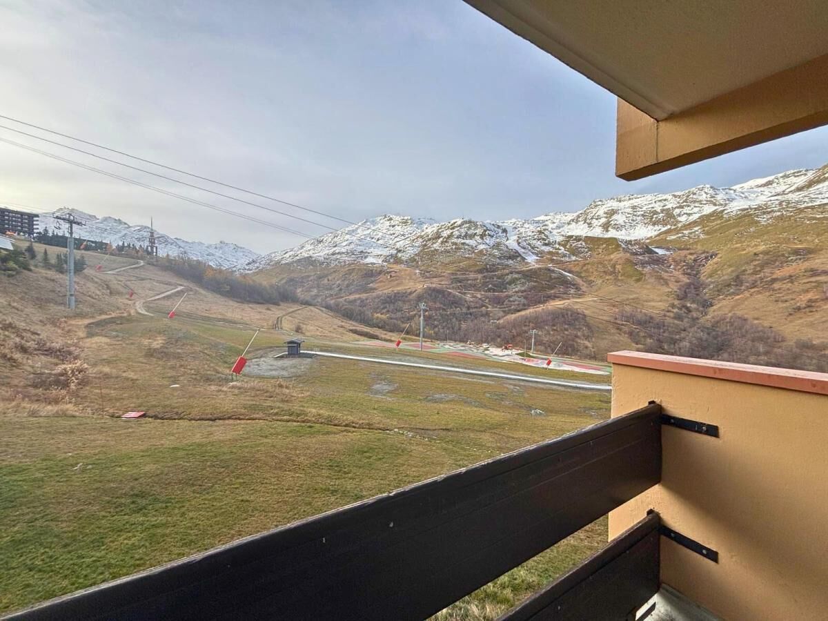Vista desde un balcón sobre un paisaje montañoso nevado, con una carretera y un edificio a lo lejos.