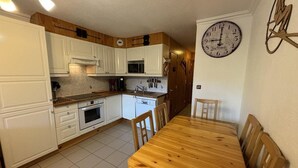 Een kleine keuken met witte kastjes, een houten eettafel en een klok aan de muur.