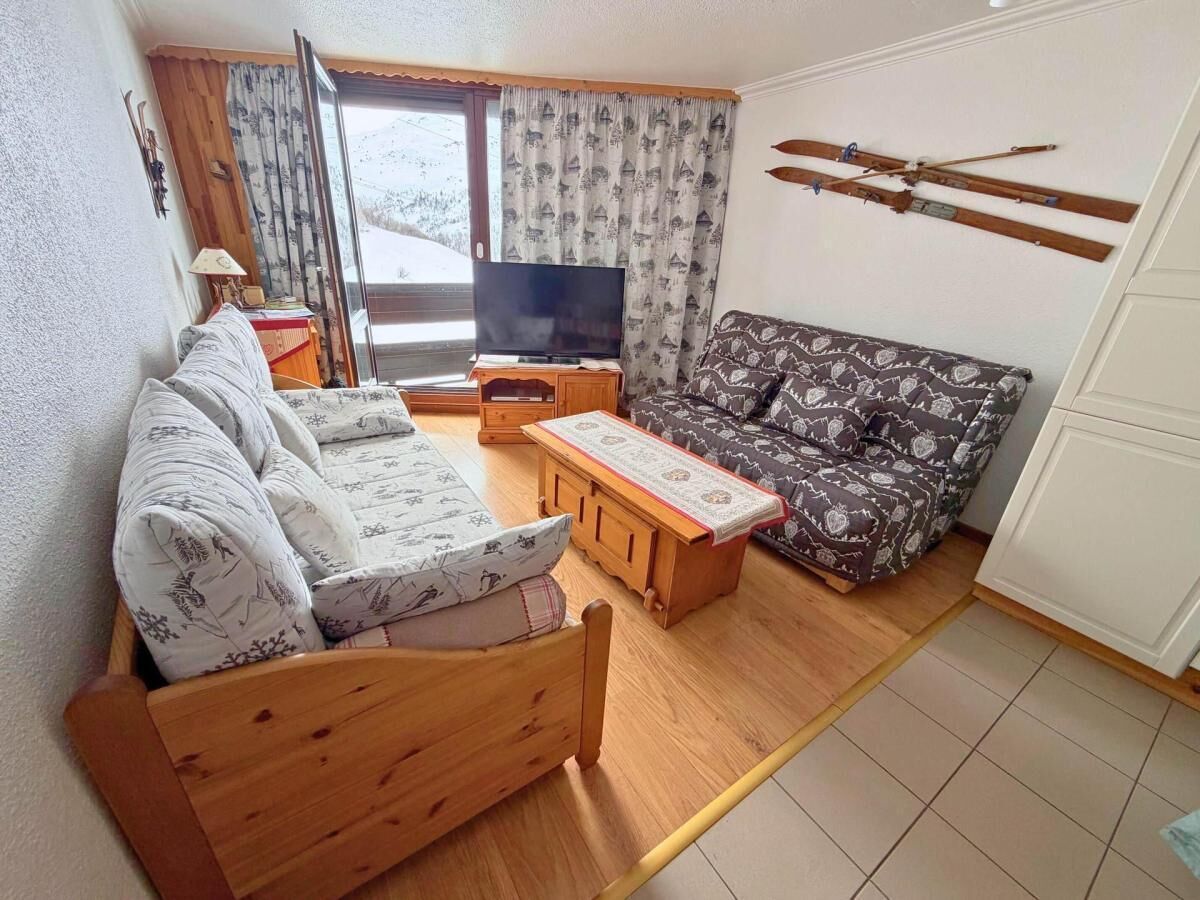 A cozy living room with a wooden sofa, a patterned sofa, a TV, and a ski rack on the wall.
