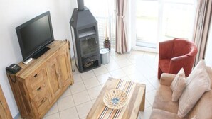 Ein Wohnzimmer mit Fernseher auf einem Holzschrank, einem Kaminofen, einem roten Sessel und einem gestreiften Couchtisch.