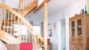 Eine Holztreppe führt zu einer oberen Ebene, ein Holzschrank mit Glastüren und ein beiges Sofa mit einem roten Kissen.