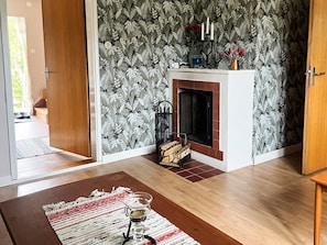 Een kamer met een open haard, behang met een patroon, een houten vloer en een vloerkleed.