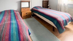 Une chambre avec deux lits simples, une commode en bois, un miroir et une table de chevet avec une lampe.