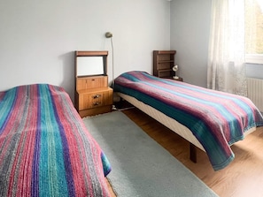 Een slaapkamer met twee eenpersoonsbedden, een houten dressoir, een spiegel en een nachtkastje met een lamp.