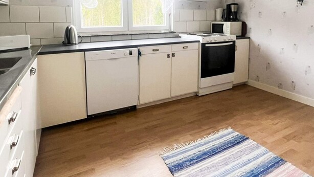 Une cuisine avec des meubles blancs, une cuisinière, un lave-vaisselle et une fenêtre avec des rideaux.