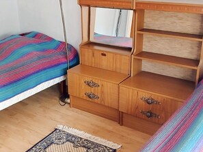 A bedroom with a bed, a wooden dresser with drawers, a mirror, and a patterned rug.