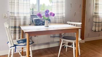A dining area with a wooden table, two white chairs, a radiator, and a window with curtains.