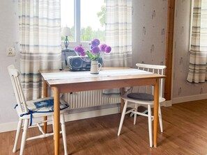 A dining area with a wooden table, two white chairs, a radiator, and a window with curtains. - 4 Person Holiday Home in Tingsryd (Tingsryd)