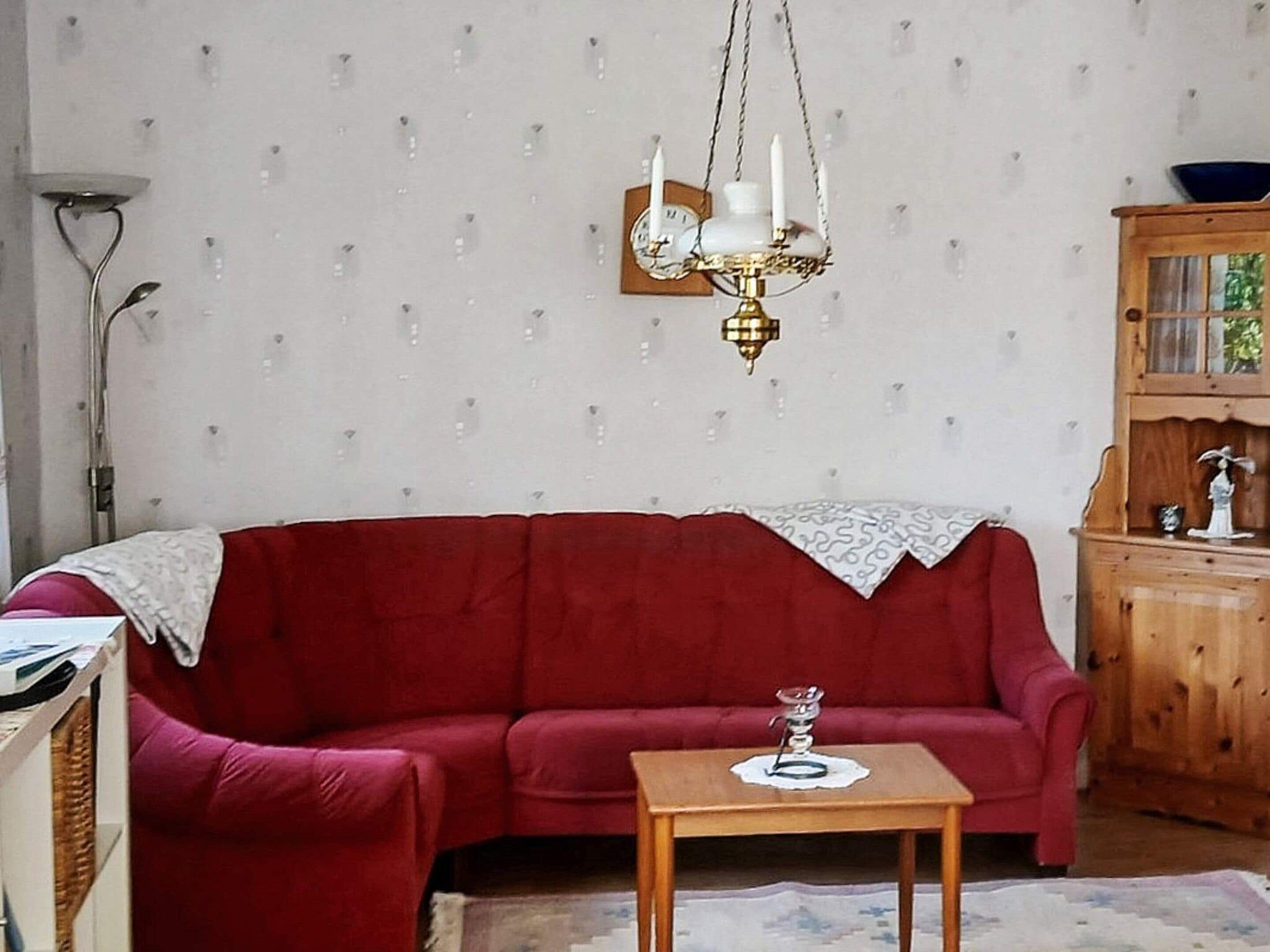 A living room with a red sofa, a wooden side table, a chandelier, and a wooden cabinet with glass doors.