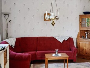 A living room with a red sofa, a wooden side table, a chandelier, and a wooden cabinet with glass doors. - 4 Person Holiday Home in Tingsryd (Tingsryd)