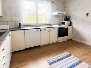 Une cuisine avec des meubles blancs, une cuisinière, un four à micro-ondes et une fenêtre avec des rideaux.
