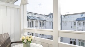 Un balcón con una mesa redonda y mobiliario de mimbre, con vistas a una hilera de edificios con fachadas blancas y balcones.