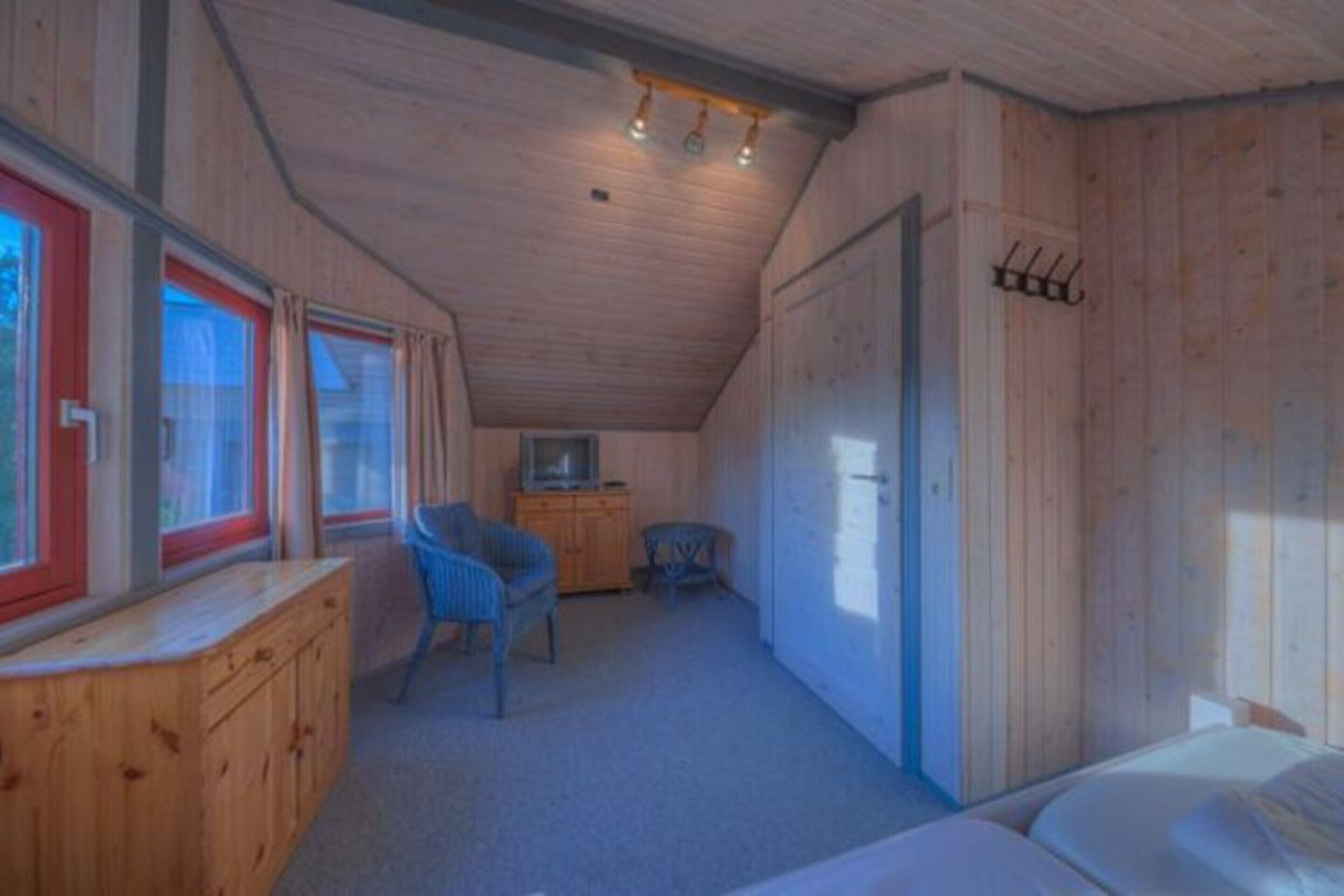 Una stanza accogliente in baita con soffitto in legno, un letto, una piccola scrivania, una sedia e un televisore.