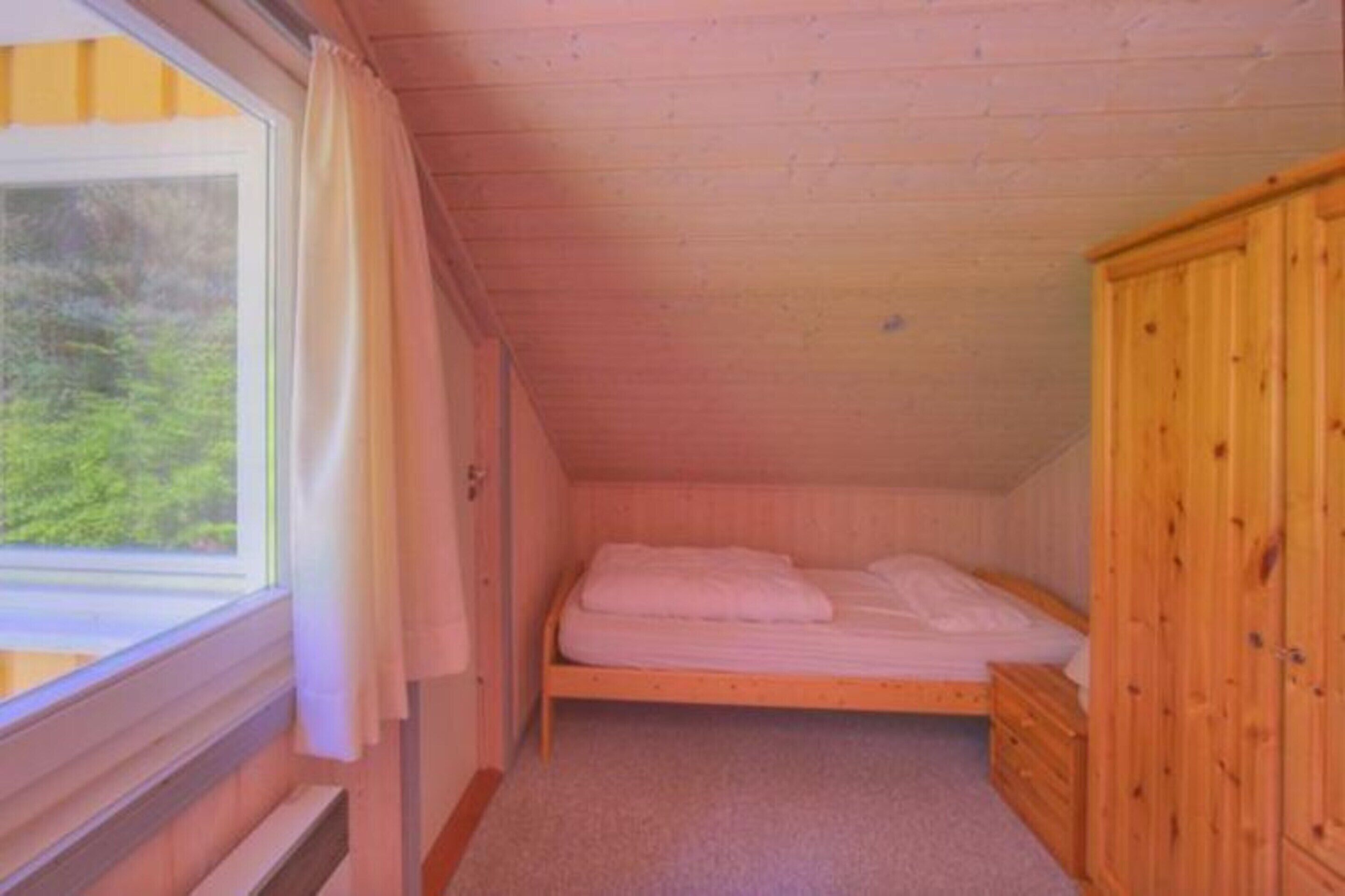 Ein kleines Zimmer mit einem Einzelbett, Holzwänden und einem Fenster.