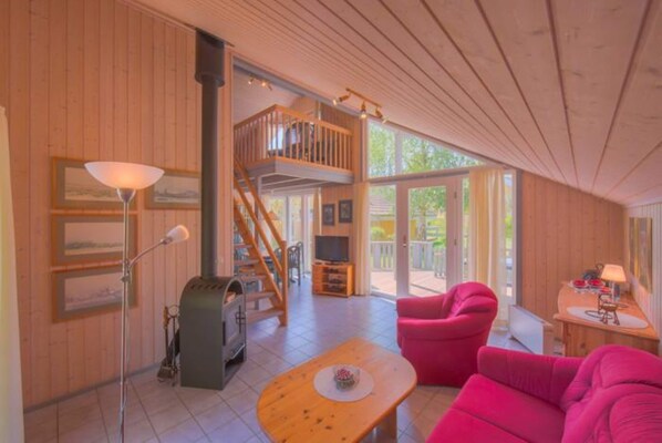 A wooden interior with a staircase, a fireplace, a television, and a pink sofa. - Exklusives Skandinavisches Ferienhaus (Mirow)
