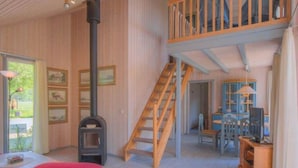 Un amplio salón con escalera de madera, chimenea y comedor con mesa y sillas.