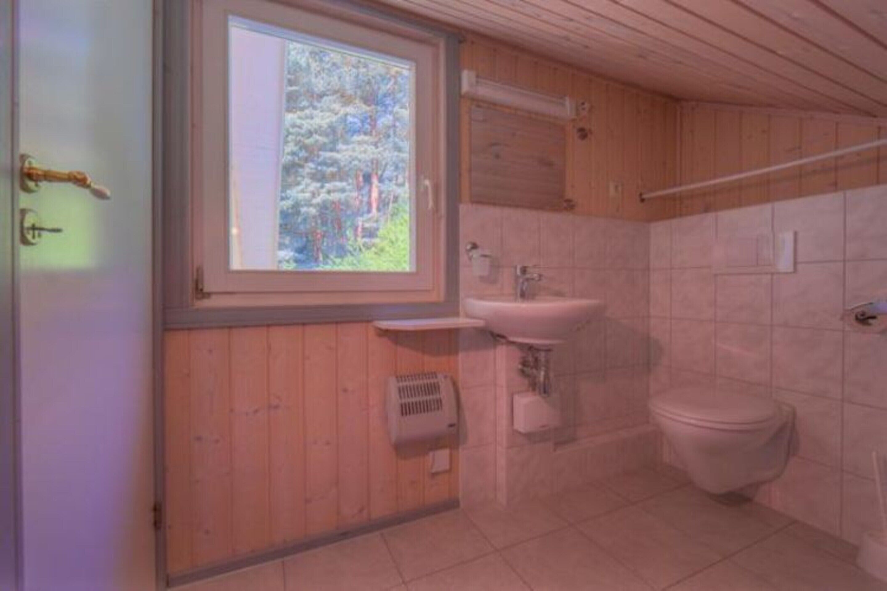 Une salle de bain avec un plancher en bois, une fenêtre donnant sur des arbres, un lavabo et des toilettes.