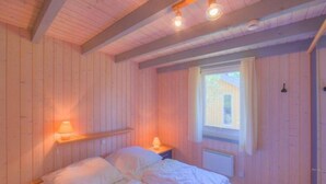 Una habitación de madera con una cama, una mesita de noche, una ventana y una lámpara fijada a la pared.