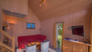 A wooden cabin interior with a red sofa, two white chairs, a wooden cabinet, and a television. - Ideales Ferienhaus fur Familien (Rechlin)