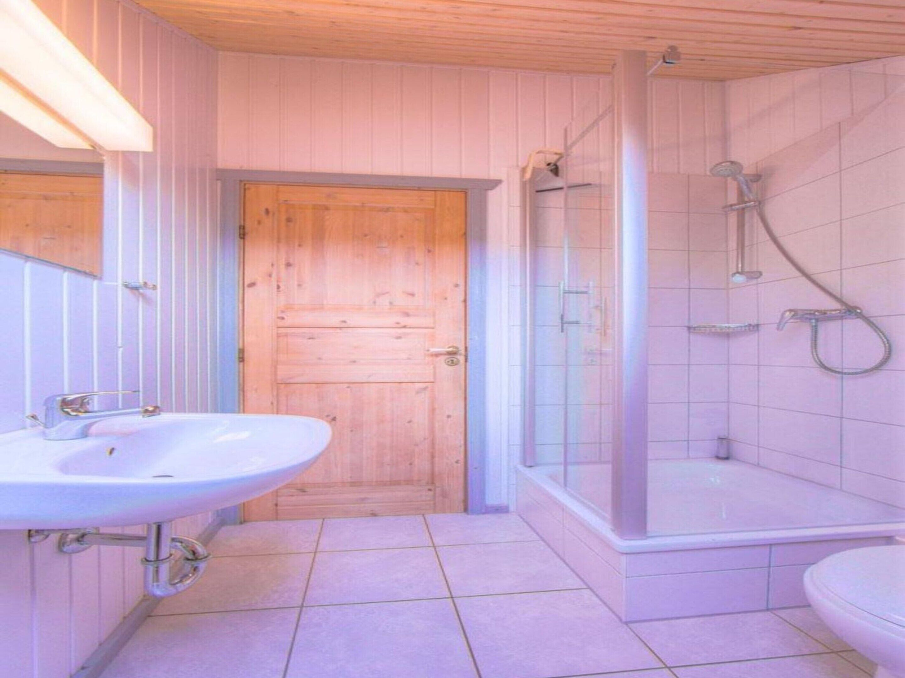 A bathroom with a wooden door, a sink, and a shower area.