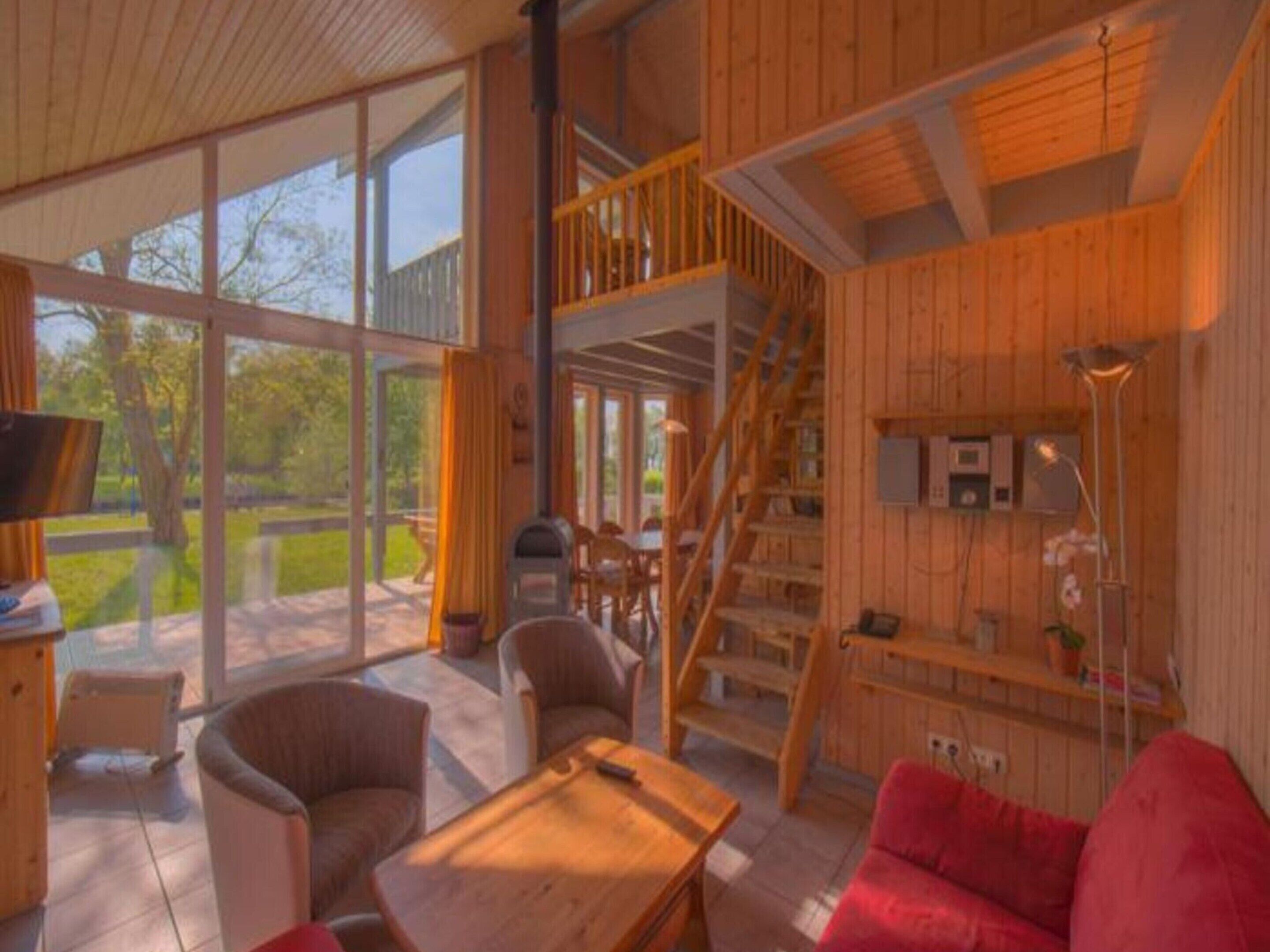 A spacious living area with a wooden interior, large windows, and a staircase leading to an upper level.