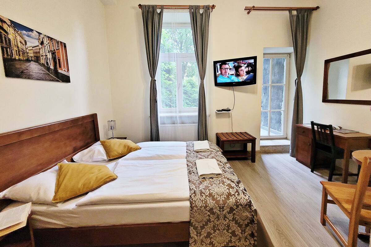 Camera d'albergo con un letto, una scrivania, una sedia, un televisore e una finestra con tende.