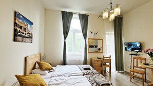 A hotel room with a bed, a desk, a chair, a TV, and a window with curtains. - DReAM Post Aparthotel (Kraków)