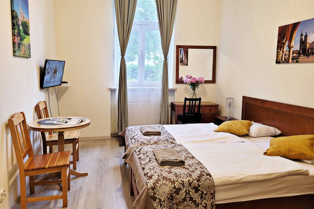 Una camera d'albergo con un letto, una scrivania, una sedia, una televisione e una finestra con tende.