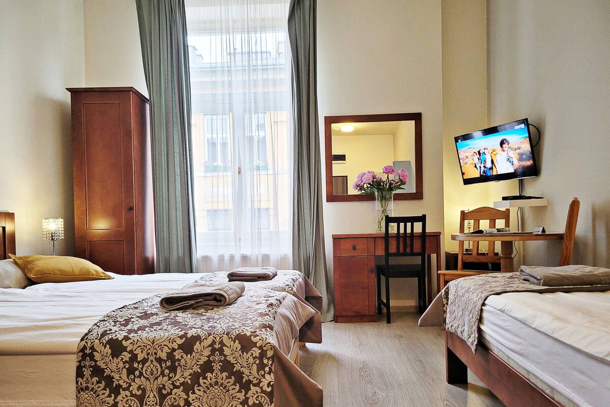 Una camera d'albergo con due letti, una scrivania, una sedia, un televisore e una finestra con tende.